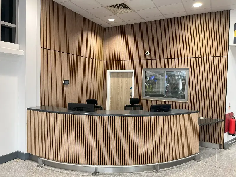 Slat panelling wrapping a curved office reception desk with a display screen behind it
