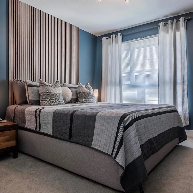 Walnut slat panelling on a blue bedroom wall beside a bed with grey striped bedding