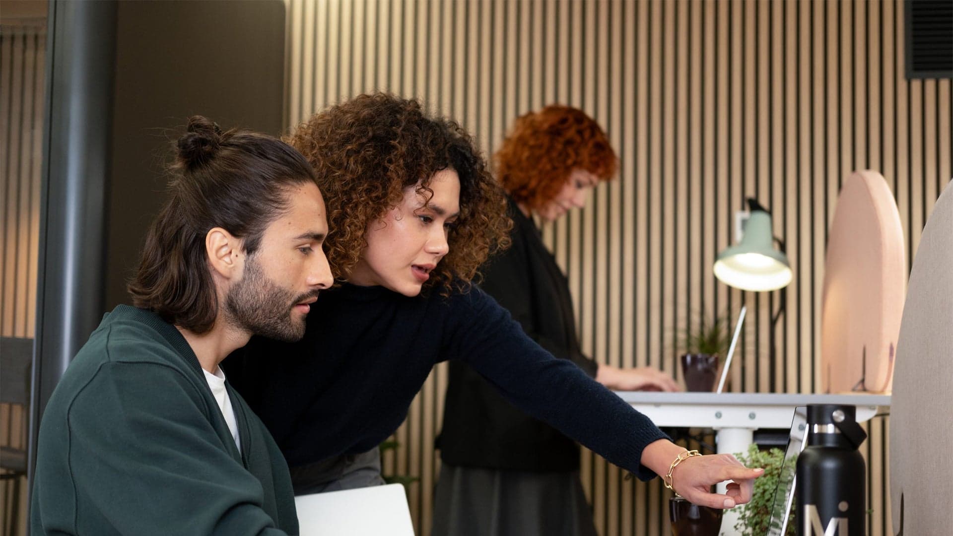 Three professionals reviewing a project at a desk against an oak slat wall